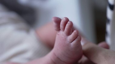 Yenidoğan küçük ayağının, yetişkin bir el tarafından sarmalanması, bebek derisinin yumuşaklığını ve ebeveyn ile çocuk arasındaki sevgi bağını vurguluyor.