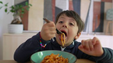 Yoğun odaklı bir çatal üzerinde spagetti çeviren küçük çocuk, sıcak bir ev ortamında yemek saatinde konsantrasyon ve kararlılık gösteriyor.