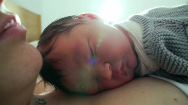 Yeni doğan bebek, annesinin göğsünde huzur içinde uyur. Yumuşak güneş ışığıyla sahneyi aydınlatır. Sıcak ve sıcak bir ortamda huzurlu ve samimi bir yakınlaşma anı yakalar.