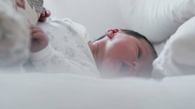 Uykulu bir ifadeyle ve yarı açık gözlerle yatakta yatan yeni doğmuş bir bebek. Bebek huzur içinde dinleniyor. Yüzlerinde yumuşak bir odaklanma, sakin ve huzurlu bir an.
