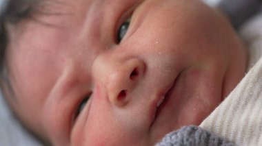 Yeni doğanın yüzüne nazik bir gülümseme, bebeğin teninin yumuşaklığı ve huzurlu ifadesiyle yakın çekim, erken yaşların narin özelliklerini ve sıcaklığını vurguluyor.