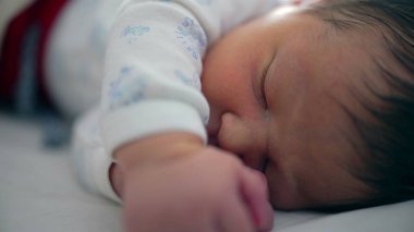 Yeni doğan bebek huzur içinde uyuyor, yüzünde ve elinde yakın planla, çocukluk döneminin huzurlu ve narin doğasını yakalıyor.