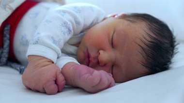 Yeni doğan bebek yumuşak bir yatakta huzur içinde uyuyor. Huzurlu bir ortamda çocukluğun huzur ve narin güzelliğini gösteriyor.