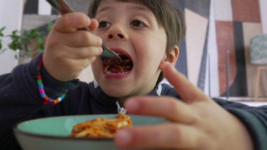 Çatalla spagetti çeviren küçük bir çocuk, göreve odaklanmış, kendini besleme konusunda konsantrasyon ve çabayı vurguluyor.