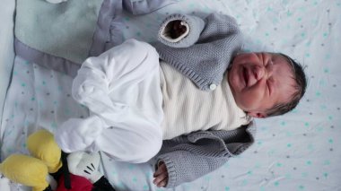 Yenidoğan bebek geriliyor ve ağlıyor, ilk hayatın ham duygularını ve fiziksel ifadelerini yumuşak, rahatlatıcı bir ortamda sergiliyor, hassasiyeti ve hassasiyeti vurguluyor.