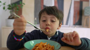 Yoğun odaklı bir çatal üzerinde spagetti çeviren küçük çocuk, sıcak bir ev ortamında yemek saatinde konsantrasyon ve kararlılık gösteriyor.