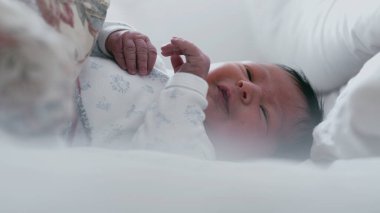 Uykulu bir ifadeyle ve yarı açık gözlerle yatakta yatan yeni doğmuş bir bebek. Bebek huzur içinde dinleniyor. Yüzlerinde yumuşak bir odaklanma, sakin ve huzurlu bir an.