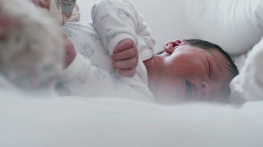 Uykulu bir ifadeyle ve yarı açık gözlerle yatakta yatan yeni doğmuş bir bebek. Bebek huzur içinde dinleniyor. Yüzlerinde yumuşak bir odaklanma, sakin ve huzurlu bir an.