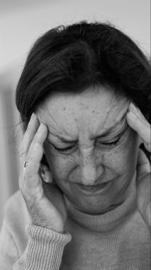 Yaşlı kadın gözlerini kapatıp şakaklarına masaj yapıyor, şiddetli baş ağrısı belirtileri gösteriyor. Onun acı ifadesine odaklan.