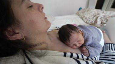 Anne, yeni doğmuş bebeği göğsünde uyurken bir yatakta dinleniyor. Erken yaşta anne ve çocuk arasındaki samimi ve rahatlatıcı bağ.