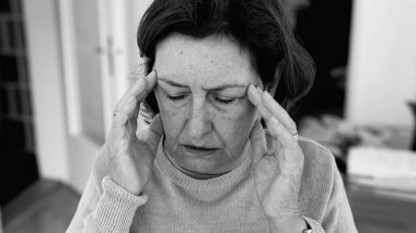 Şiddetli baş ağrısı olan yaşlı bir kadın, elleri şakaklara baskı yapıyor, derin konsantrasyon ve zihinsel gerginlik. Yaşlanan cilt ve yüz hatları, stres yoğunluğu, duygusal acı.
