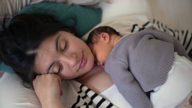 Anne yeni doğmuş bebeğini göğsünde tutarken huzur içinde dinleniyor. Sıcak bir ev ortamında kestirirken hassas bir anı yakalıyor. Yürek ısıtan bir sahne yaratıyor.
