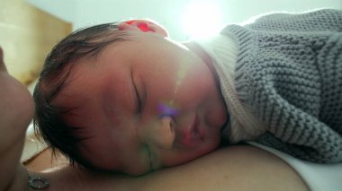 Yeni doğan bebek, annesinin göğsünde huzur içinde uyur. Yumuşak güneş ışığıyla sahneyi aydınlatır. Sıcak ve sıcak bir ortamda huzurlu ve samimi bir yakınlaşma anı yakalar.