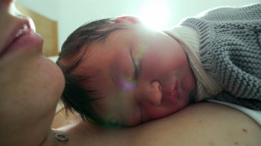 Yeni doğan bebek, annesinin göğsünde huzur içinde uyur. Yumuşak güneş ışığıyla sahneyi aydınlatır. Sıcak ve sıcak bir ortamda huzurlu ve samimi bir yakınlaşma anı yakalar.