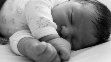 Uyuyan bir bebeğin siyah-beyaz yakın çekimi, erken çocukluğun ve huzurlu dinlenmenin hassas ve zamansız doğasını vurguluyor.