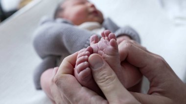 Ebeveynler yeni doğan bebekleri nazikçe kucaklar, küçük ayakları, sevgi ve özen göstererek besleyici bir çevrede, ebeveynler ve çocuklar arasındaki yakın bağı vurgular.