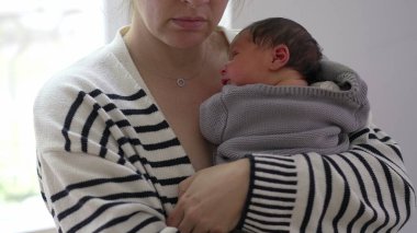 Anne, uyuyan bebeği göğsüne bastırıyor, rahat bir battaniyeye sarılıyor, sakin ve huzurlu bir ortamda hassas ve samimi bir yakınlaşma anı sergiliyor.