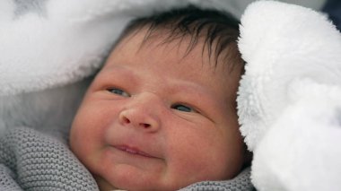 Yeni doğmuş bebek rahat bir battaniyeye sarılmış hafif bir sırıtışla, içerik gösteren ama biraz da eğlendirici bir ifade, erken yaşamda sıcak ve güvenli bir anı yakalıyor.