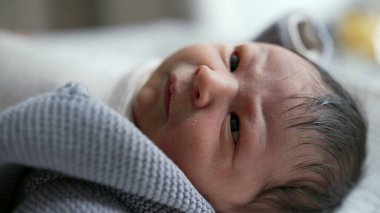 Yeni doğmuş bir bebeğin dinlenme ve geniş gözlerle bakma görüntüsü, erken yaşlardaki merak ve masumiyet anları, besleyici bir çevrede sıcaklık ve konforla çevrili.