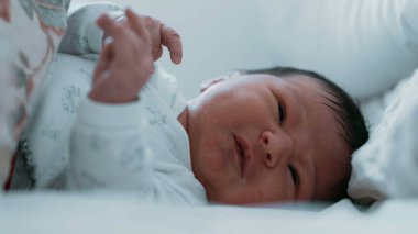 Yeni doğmuş bir bebek yatakta yatarken yakından ağlıyor. Bebeğin yüzü sıkıntılı, gözleri kapalı ve ağzı açık, rahatsız edici.