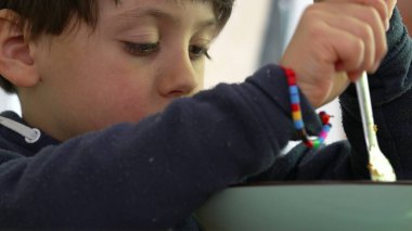 Küçük çocuk spagettiyi çatalla çevirmekle meşgul, kararlı bir ifadeyle, sıcak, ev ortamında yemek saatinde konsantrasyon ve çabayı vurguluyor.