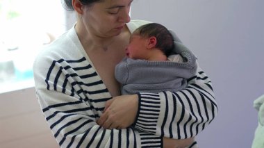 Anne, yumuşak bir battaniyeye sarılı olarak yeni doğan bebeğine bakıyor. Bebeği huzurlu ve sevgi dolu bir kucaklama içinde kucaklıyor. Derin bir bağ ve özen anının altını çiziyor.