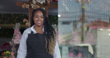 Çiçekçinin önünde gülümseyen kendine güvenen çiçekçi, kameraya bakıyor. Çiçek süslemeleri ve hediyelerle dolu şehir butiğinin sıcaklığı ve gururuyla.