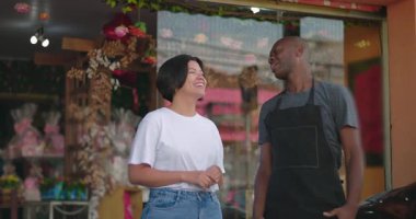 Çiçekçinin önünde iki dükkan sahibi arasında dostça bir sohbet, gülümseyen ve gevşemiş vücut dili, canlı perakende dekorasyonları.