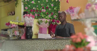 Çiçekçi dükkanında gül buketleri, hediye eşyalar ve renkli ve misafirperver iş arka planında dekoratif çiçek duvarı ile notlar alıyor.
