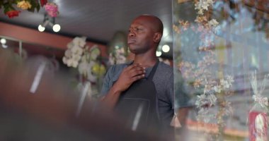 Belirsiz bir ifadeyle kafasını kaşıyan Afrikalı Amerikalı çiçekçi. Çiçek sergisi yakınlarındaki dükkan operasyonlarını yansıtan girişimci.