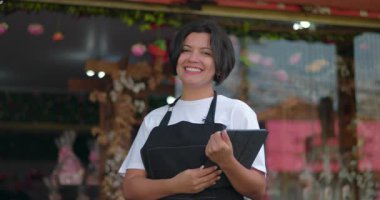 Çiçekçi dükkanının önünde güvenle dikilirken elinde tabletle mutlu bir çiçekçi vardı. Pozitif tutumla iş işlerini yürütmeye hazırdı.