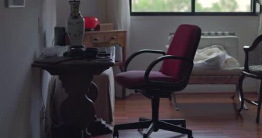 Boş ev ofisi, ahşap masaya bakan kırmızı sandalye, elektronik cihazlar ve masa üzerindeki dekoratif lamba, rahat odanın penceresinden içeri gün ışığı giriyor.