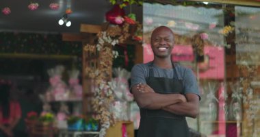 Çiçekçi dükkanının önünde kollarını kavuşturarak gülümseyen, çiçekçi dükkanının önünde güvenle duran, neşeli ve gururlu.