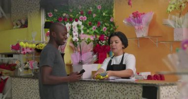 Çiçekçi, çiçek buketi hediye, gül ve dekoratif düzenlemelerle dolu canlı çiçekçide gülümseyen müşteriye veriyor.