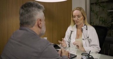 Modern klinik ofisinde reçeteli muayene sırasında orta yaşlı erkek hastaya ilaçları açıklayan kadın doktor.