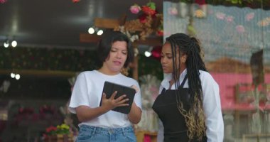 Çiçekçi ve iş ortağı planlarını tablet kullanarak tartışıyor, çiçekçi dükkanının dışındaki düzenlemeleri ve dekorasyonları gözden geçiriyorlar.