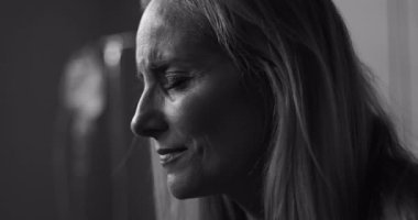 Duygusal ifadeyle aşağıya bakan, klinik ortamda incinebilirlik ve acıyı yakalayan siyah beyaz bir kadın.