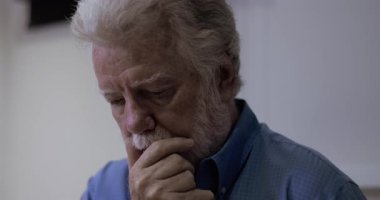 Son sınıf öğrencisi, düşünceli bir ifadeyle çenesini dinlendirirken, derin düşüncelere dalmış, sessiz bir odada aşağıya bakıyor.