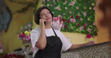 Çiçekçi telefonda konuşurken tezgahta notlar alıyor, çiçekçinin içindeki iş detaylarını yönetiyor.