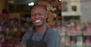 Kollarını kavuşturmuş gülümseyen çiçekçi renkli çiçekçinin önünde duruyor, kendine güvenen ve dost canlısı bir iş adamı dükkanın önünde poz veriyor.