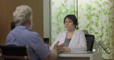 Klinikteki muayene sırasında doktora semptomları açıklayan hasta, el hareketleriyle ve sağlık hizmetleriyle ilgili konuşmalarla meşgul.