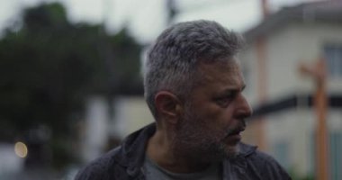 Orta yaşlı bir adam endişeli bir ifadeyle, gergin duruşu ve sokak ortamında duygusal ağırlığıyla bir kenara bakıyor.