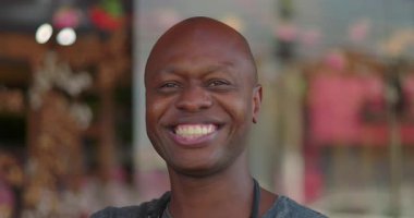 Çiçekçi dükkanının dışında gülümseyen bir portre, neşeli ve kendinden emin bir ifade, arka planda çiçek dekoru olan sıcak ve davetkar bir atmosfer