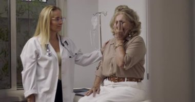 Yaşlı bayan hasta zor haberler alıyor ve klinik muayene odasında duygusal bir anda kadın doktorun kucaklamasıyla teselli buluyor.