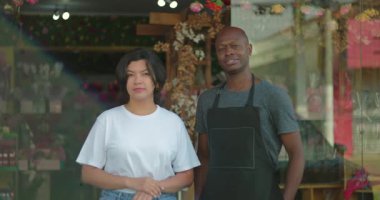 Çiçekçinin önünde duran çiçekçi ekibi, mağazanın önünde poz veren kadın ve erkek, kendine güvenen ifade ve enerjik dükkan geçmişi