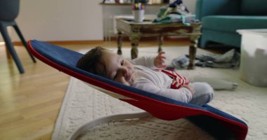 Bebek bir fedaide yatıyor, gülümsüyor ve mutlu görünüyor, rahat bir ev ortamında rahatlık ve rahatlığın tadını çıkarıyor, çocukluk yıllarının masumiyetini ve neşesini vurguluyor.