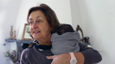 Büyükannem yeni doğmuş bir bebeği omzunda tutuyor, bebeği nazikçe okşuyor ve rahatlatıyor, şefkatli ve samimi bir sevgi ve ilgi anı yakalıyor.