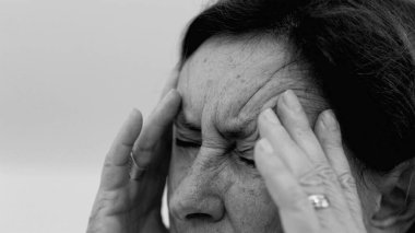 Yaşlı kadın yakın plan, gözleri kapalı, iki eli şakaklarına bastırıyor, derin kırışıklıklar ve acı dolu ifade, şiddetli stres ya da baş ağrısı