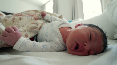 Çiçekli bir battaniyenin altında dinlenen yeni doğmuş bebek, çevresini keşfederken yüzünü buruşturuyor ve işaret ediyor, hayatın ilk ayı ve erken gelişim kilometre taşları.