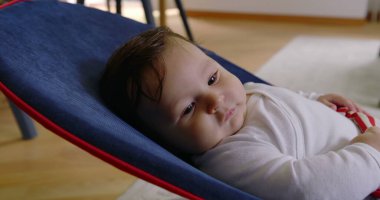 Bebek bir fedaide uzanıyor, sakince yukarı bakıyor, rahat bir ev ortamında rahatlığın ve rahatlığın tadını çıkarıyor, çocukluk yıllarının masumiyetini ve huzurunu gösteriyor.